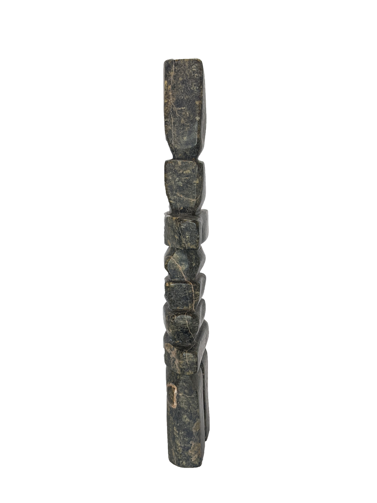 A tall, rigid inukshuk composed of stark, straight lines. Six slabs in varying lengths make up the body, with the legs and head being very tall by comparison. The stone is striking brown and green.