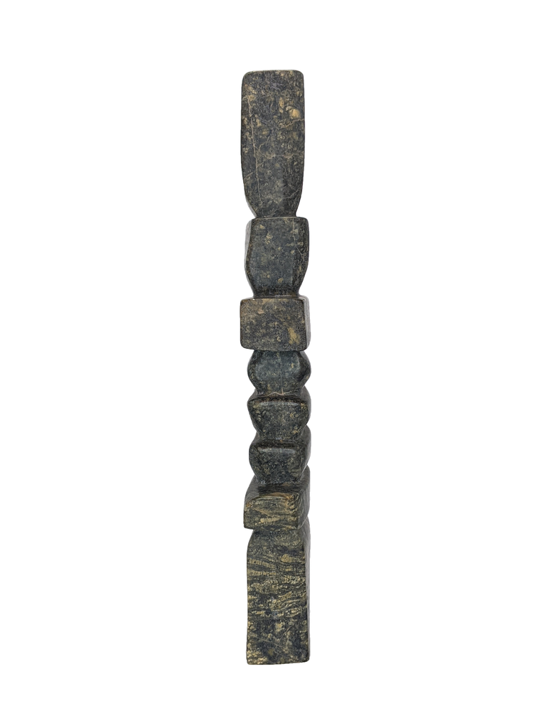 A tall, rigid inukshuk composed of stark, straight lines. Six slabs in varying lengths make up the body, with the legs and head being very tall by comparison. The stone is striking brown and green.