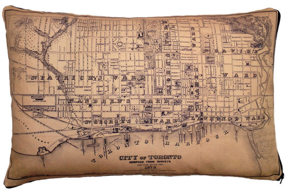 This large pillow features a vintage map of Toronto. The map is printed in black on a tan background. It shows the major wards of the city, the harbor front, and a few prominent landmarks. 