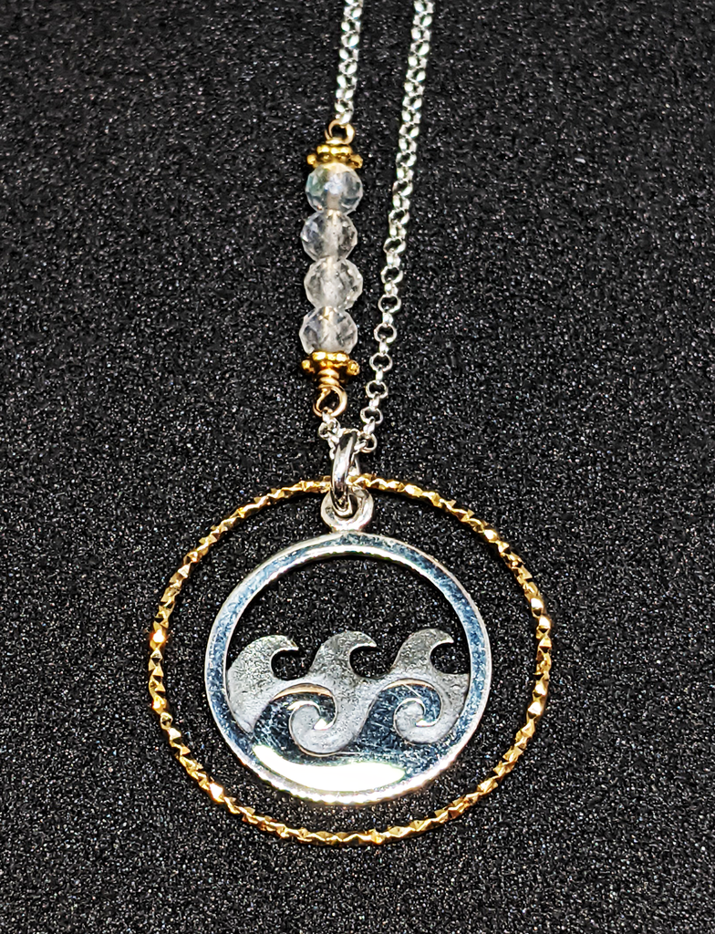 Silver chain with 5 coloured beads in middle of chain attached with gold chain links that look like flowers. Pendent is a gold ring that has triangle ridges. Inside gold ring is a silver ring with 2 silver waves and 4 grey waves behind them. 