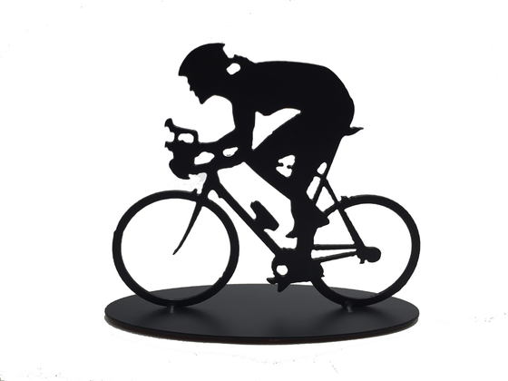 This metal sculpture shows the matte black silhouette a female cyclist hunched forward over their handle bars. She faces left and stares forward intently. The bike design is slightly simplified, and the wheels have no spokes. The piece stands on an oval base.