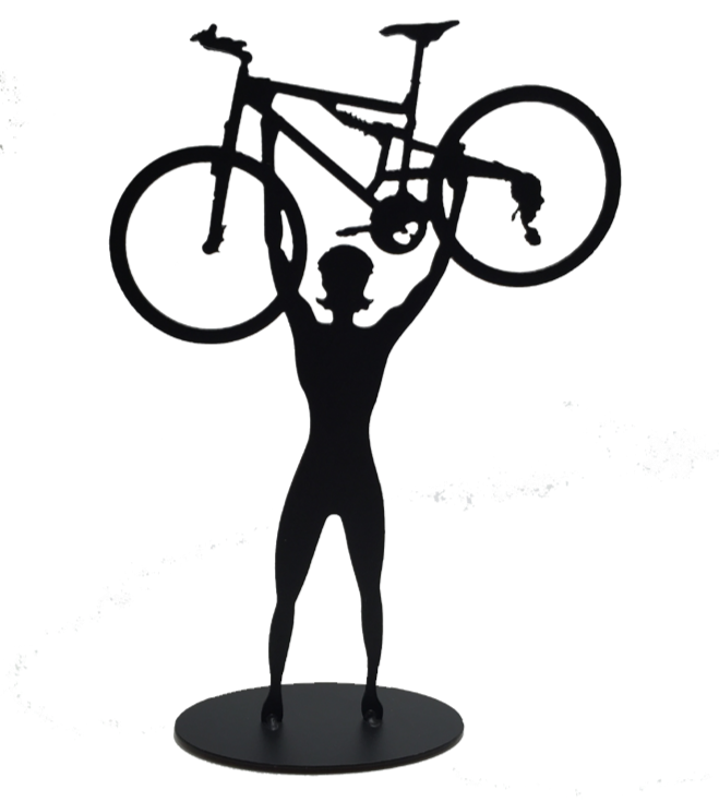 This metal sculpture shows the matte black silhouette a female cyclist facing the viewer. She holds a mountain bike triumphantly above her head. The bike design is slightly simplified, and the wheels have no spokes. The piece stands on a small oval base.