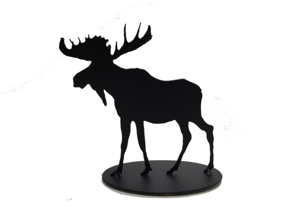 This metal sculpture shows the matte black silhouette of a moose. It has a full rack of antlers and a pronounced dewlap. Its strong shoulders contrast with its slender legs. Careful detailing along the edges give this piece a strong sense of realism. It stands on an oval base.