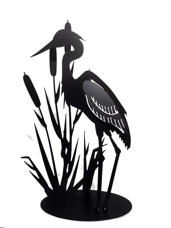 This metal sculpture shows the matte black silhouette of a heron standing with cattails. The wing of the heron has been partially punched out of the metal, and bent to render the bird in 3D. Individual wing feathers are visible. The cattails are cut very delicately and in lifelike shape and proportion to the heron. The piece sits on an oval base.