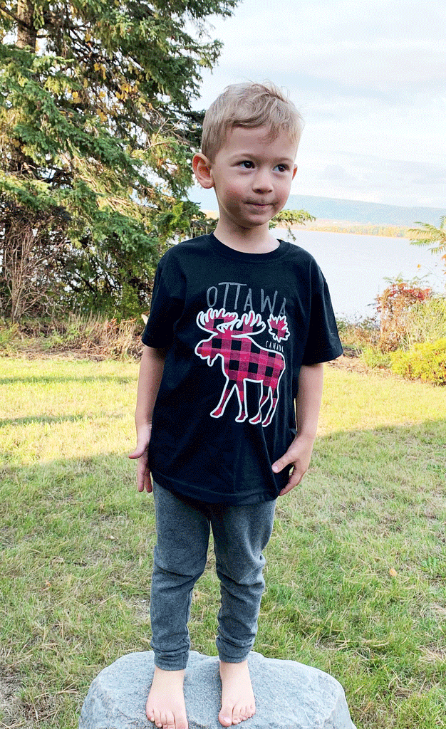 A black shirt. In the middle is a white moose and a small maple leaf outline with a plaid red and black pattern. At the top is written "Ottawa", and underneath the maple leaf is written "Canada".