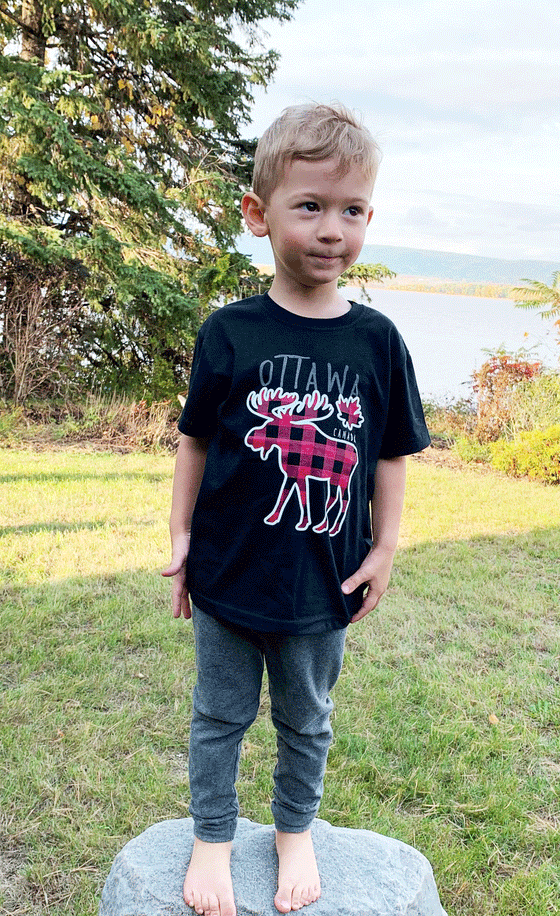 A black shirt. In the middle is a white moose and a small maple leaf outline with a plaid red and black pattern. At the top is written "Ottawa", and underneath the maple leaf is written "Canada".
