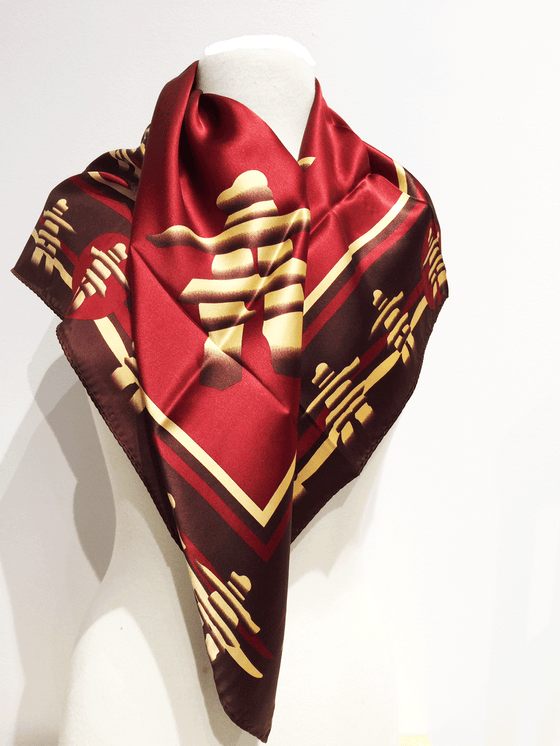 Pictured here is a burgundy silk scarf with yellow and brown accents. Featured on the scarf is the stately Canadian Inukshuk.