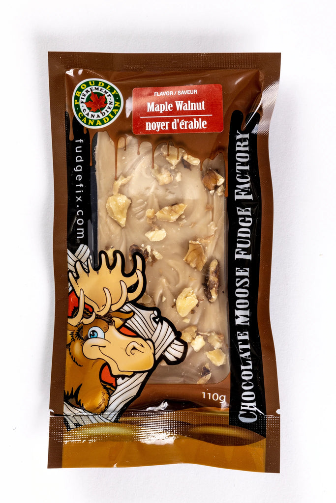 Rectangular Fudge Bar made in Canada Inside of a plastic package. There is a cartoon Moose on the cover of the package, and big writing saying 'Chocolate Moose Fudge Factory'. Flavor of the fudge is labeled Maple Walnut. Fudge is light brown maple with pieces of walnuts on top of it. 
