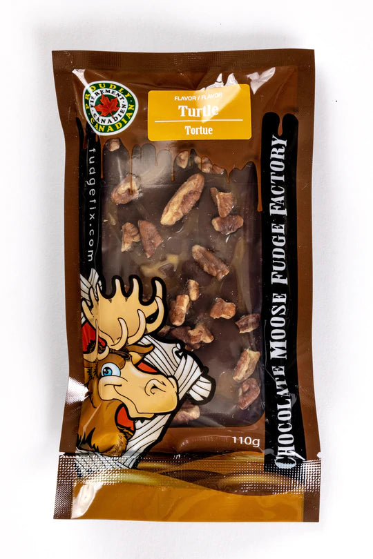 Rectangular Fudge Bar made in Canada Inside of a plastic package. There is a cartoon Moose on the cover of the package, and big writing saying 'Chocolate Moose Fudge Factory'. Flavor of the fudge is labeled Turtle. Fudge is chocolate with some caramel. Pieces of pecans on top of the fudge.