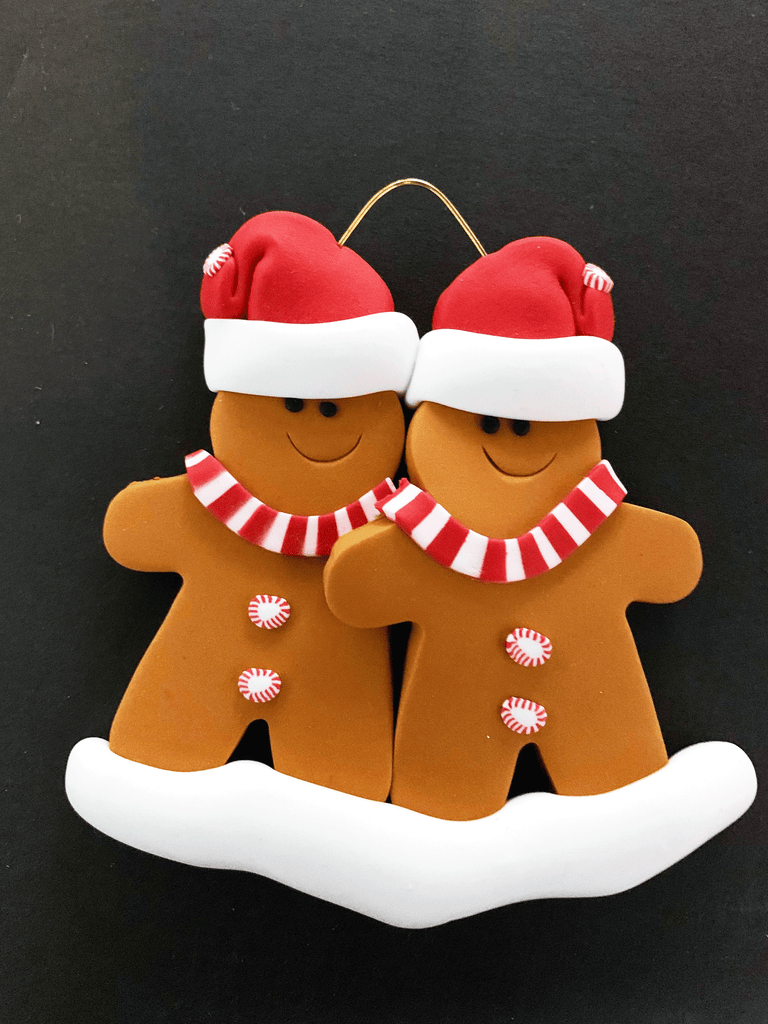 Two smiling gingerbread men stand side by side wearing a red Santa hat, red and white mints as buttons, and a red and white striped scarf.