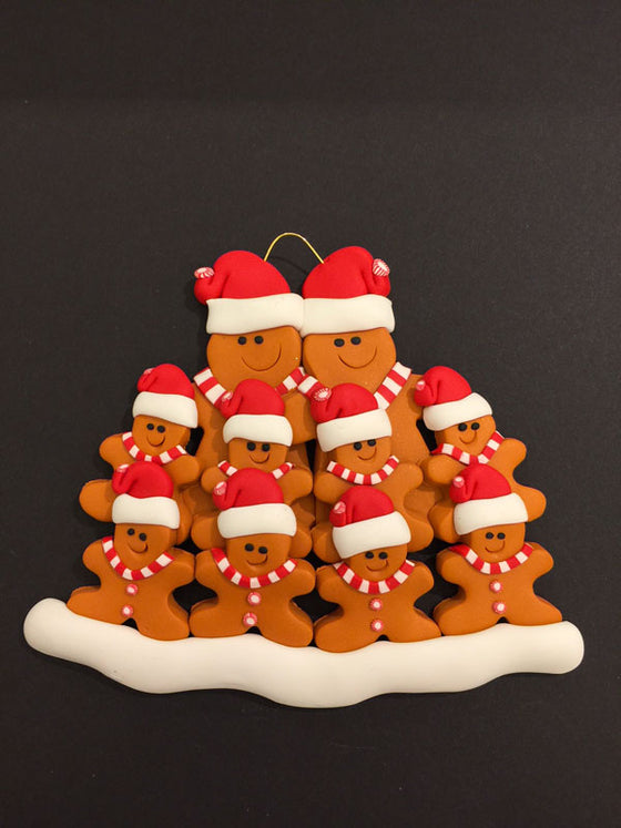 Two smiling gingerbread men stand side by side wearing a red Santa hat, red and white mints as buttons, and a red and white striped scarf. Eight similarly dressed gingerbread children stand in front of the larger figures.
