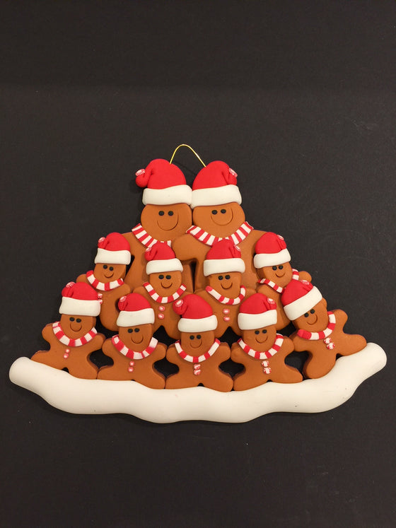 Two smiling gingerbread men stand side by side wearing a red Santa hat, red and white mints as buttons, and a red and white striped scarf. Nine similarly dressed gingerbread children stand in front of the larger figures.