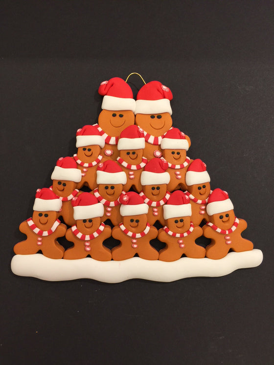 Two smiling gingerbread men stand side by side wearing a red Santa hat, red and white mints as buttons, and a red and white striped scarf. Twelve similarly dressed gingerbread children stand in front of the larger figures.