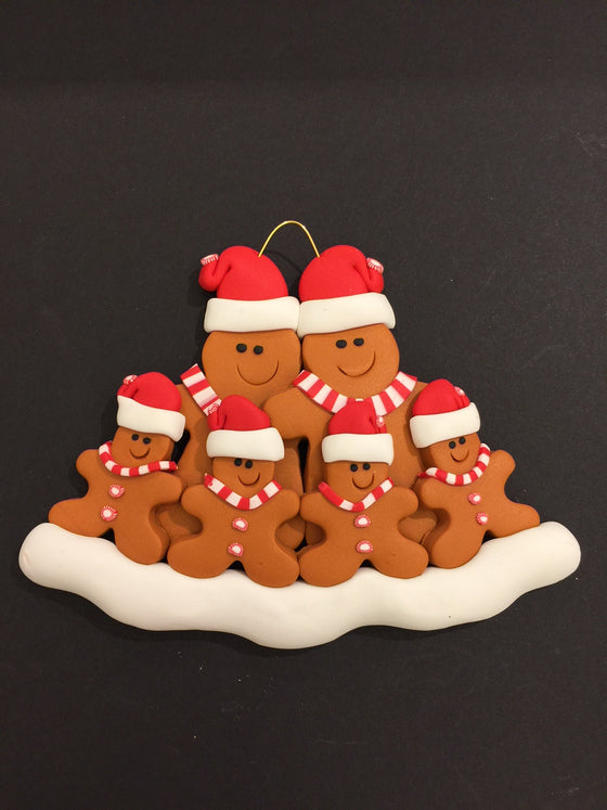 Two smiling gingerbread men stand side by side wearing a red Santa hat, red and white mints as buttons, and a red and white striped scarf. Four similarly dressed gingerbread children stand in front of the larger figures.