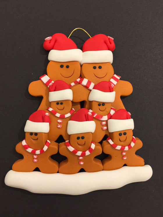 Two smiling gingerbread men stand side by side wearing a red Santa hat, red and white mints as buttons, and a red and white striped scarf. Five similarly dressed gingerbread children stand in front of the larger figures.