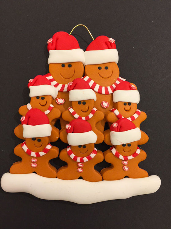 Two smiling gingerbread men stand side by side wearing a red Santa hat, red and white mints as buttons, and a red and white striped scarf. Six similarly dressed gingerbread children stand in front of the larger figures.