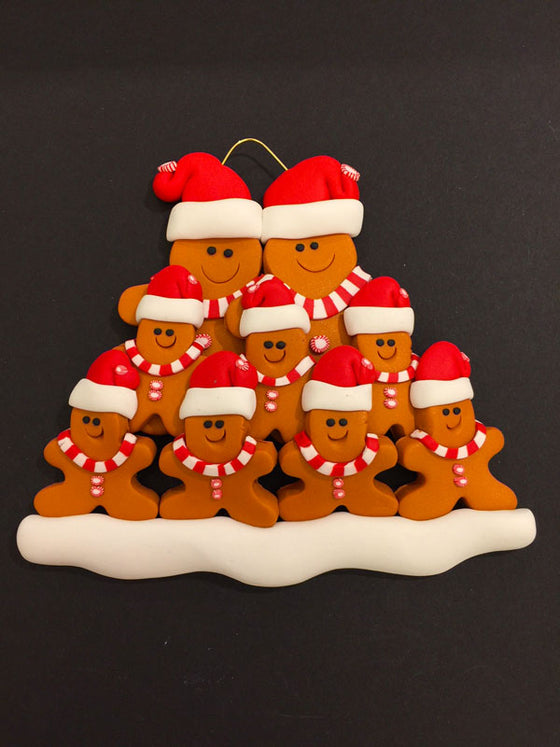Two smiling gingerbread men stand side by side wearing a red Santa hat, red and white mints as buttons, and a red and white striped scarf. Seven similarly dressed gingerbread children stand in front of the larger figures.