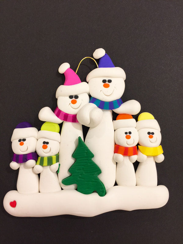 A family of six happy snowmen. The large snowmen hold hands and are dressed in pink and blue hats and scarves. The smaller snowmen wear purple, green, orange, and yellow. In front of the group sits a small Christmas tree.