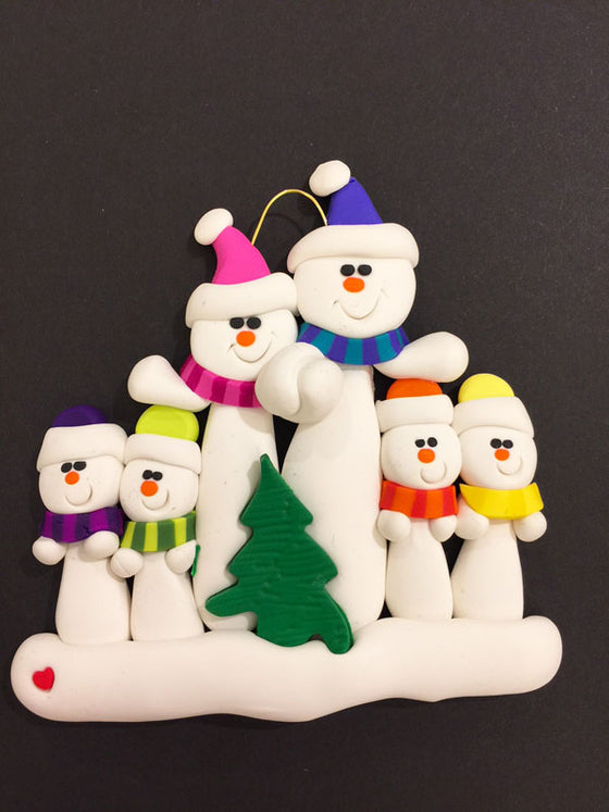 A family of six happy snowmen. The large snowmen hold hands and are dressed in pink and blue hats and scarves. The smaller snowmen wear purple, green, orange, and yellow. In front of the group sits a small Christmas tree.