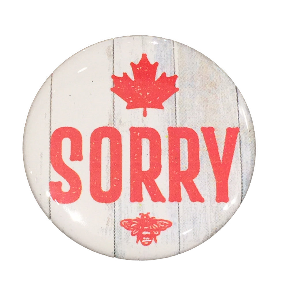 This magnet shows the word “Sorry” in bold red text on a pale, wood-textured background. A red maple leaf is printed above the text, and a small red bee—the artist’s mark—printed below it.