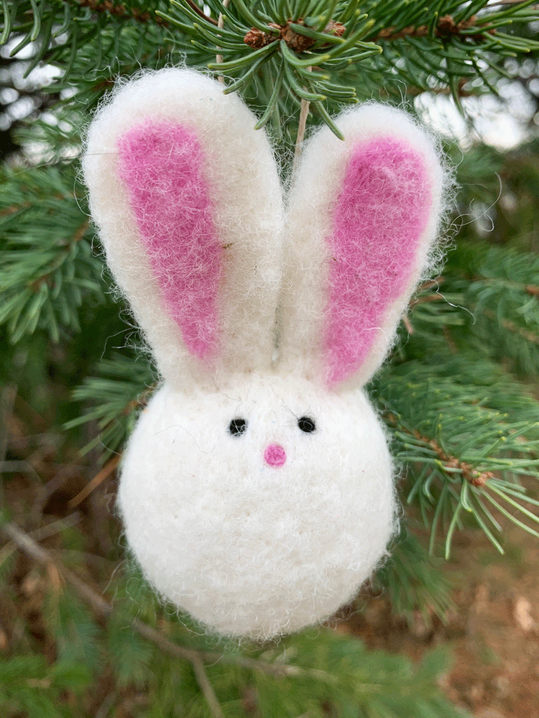 A white felted wool bunny. It has a round body with two small black eyes and a pink nose. Two enormous ears with pink insides emerge from the top.