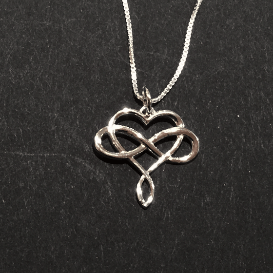 A sterling silver infinity symbol intertwined with a heart hangs from a silver chain. The infinity symbol crosses the middle of the heart horizontally. The bottom of the heart twists to form a loop reminiscent of the infinity symbol.
