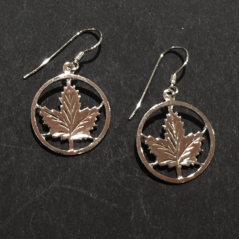 Two small sterling silver maple leaf earrings sit on a black background.  The maple leaves are enclosed by a silver circle. The earring hooks attach to the top of the circle.