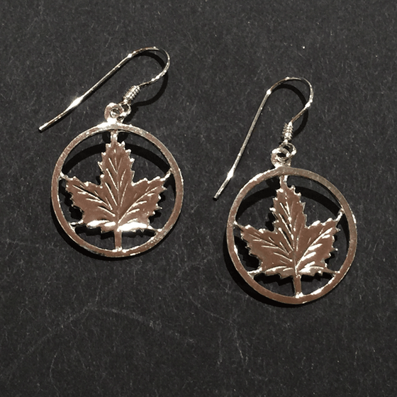 Two small sterling silver maple leaf earrings sit on a black background.  The maple leaves are enclosed by a silver circle. The earring hooks attach to the top of the circle.