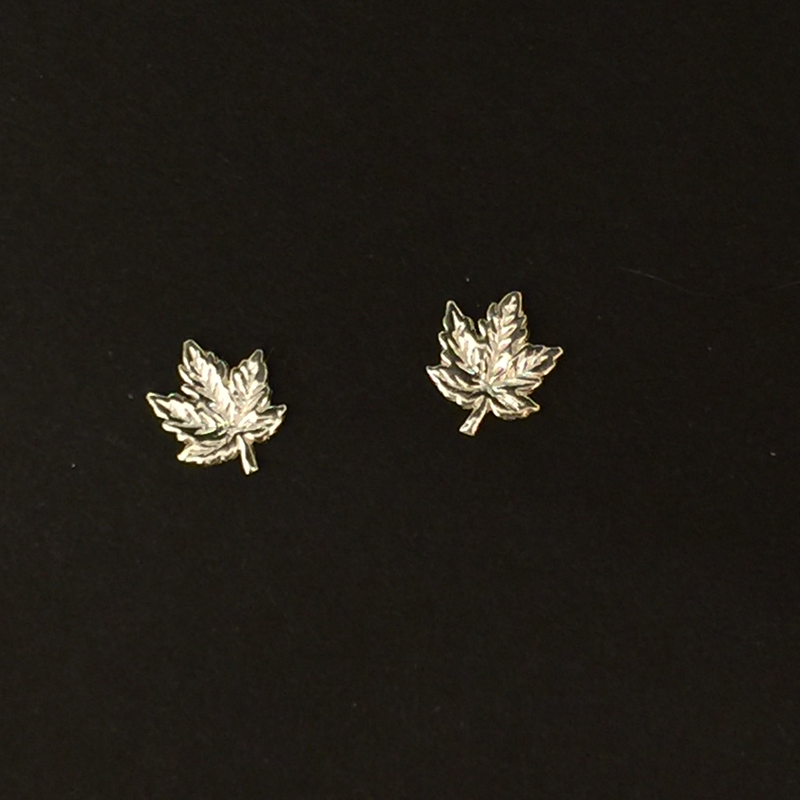 Two small sterling silver maple leaf earrings sit on a black background.  The earring backs cannot be seen.