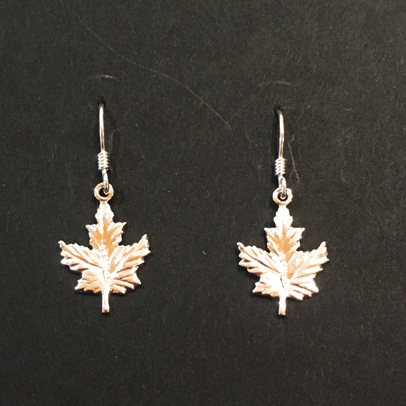 Two small sterling silver maple leaf earrings sit on a black background.  The earrings have silver earring hooks attached to the top point of the leaf charm.