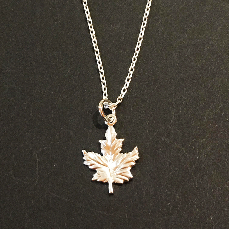 A small sterling silver maple leaf on a silver chain sits on a black background. The maple leaf charm is attached to the chain at its top point.
