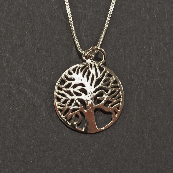 A sterling silver tree charm hangs from a silver chain on a black background. The tree is contained within a hoop. The tree’s numerous thin branches radiate outward and fuse with the outer hoop. 