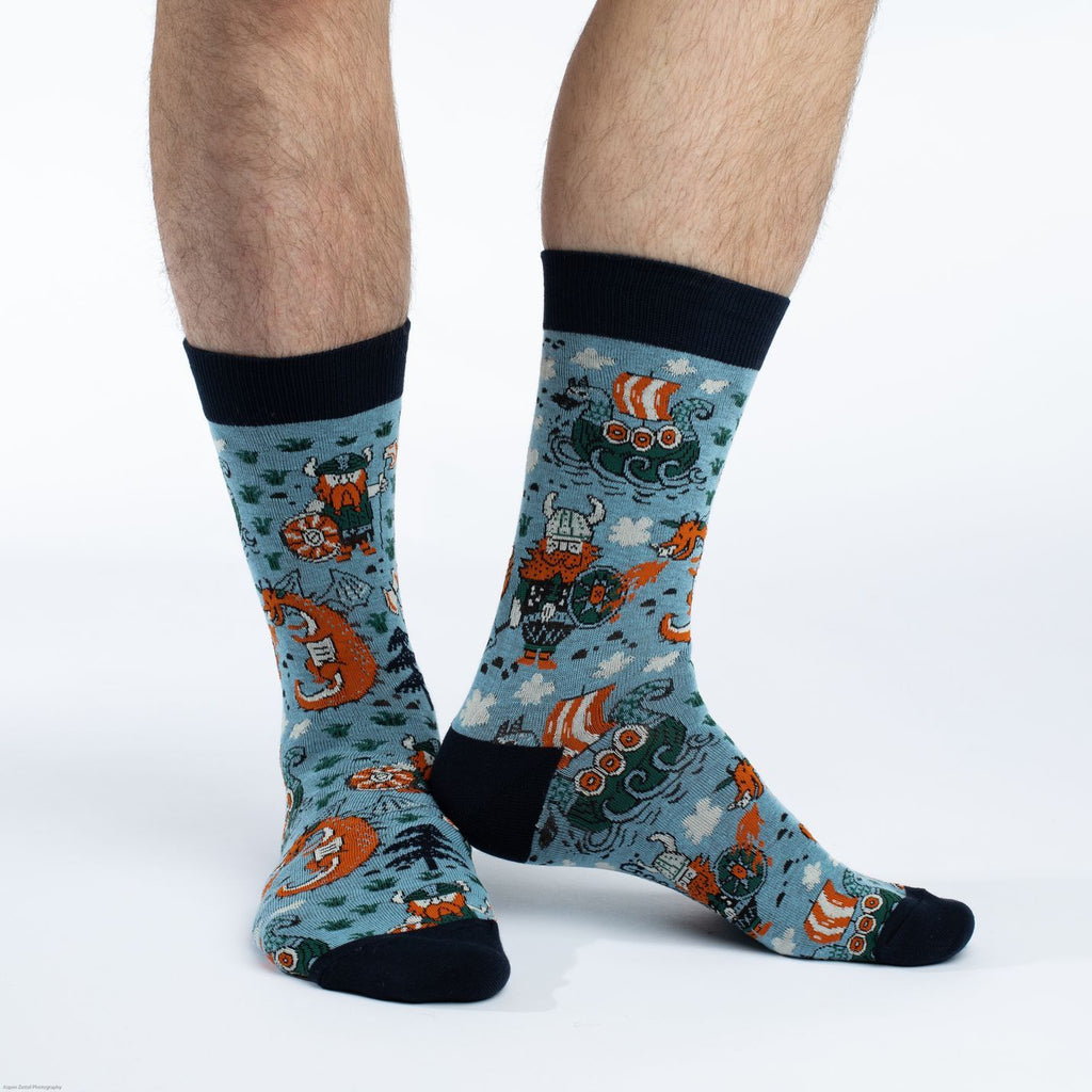 These fun socks feature viking sailing ships, great red dragons spitting fire at vikings sporting great red beards, round shields, and horned helmets on a light blue background. The toe, heel, and rim of the sock are black. Spandex added to the 85% cotton blend gives the socks the perfect amount of stretch to hug your feet.