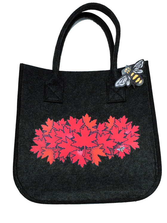This small dark grey felt bag has two overhead handles and features an art print of a spray of red maple leaves. At the bottom right of the picture is the artists mark—a small picture of a bee.