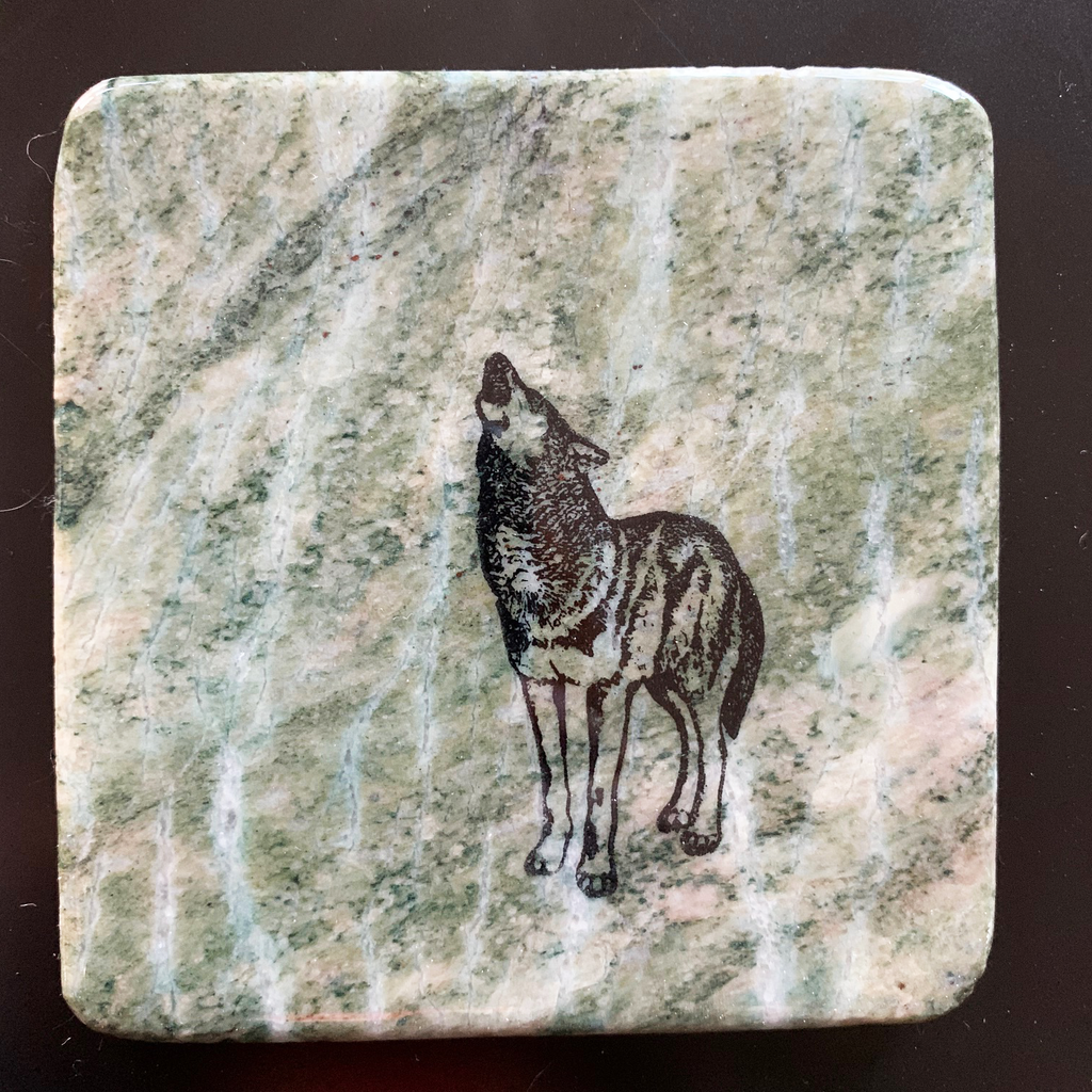 This coaster features the image of a wolf standing while howling into the sky. The image is on a piece of canadian shield marble with mineral lines running through in unique colours, lines, and patterns. The coaster is finished with a clear coat, giving it a shiny finish. 