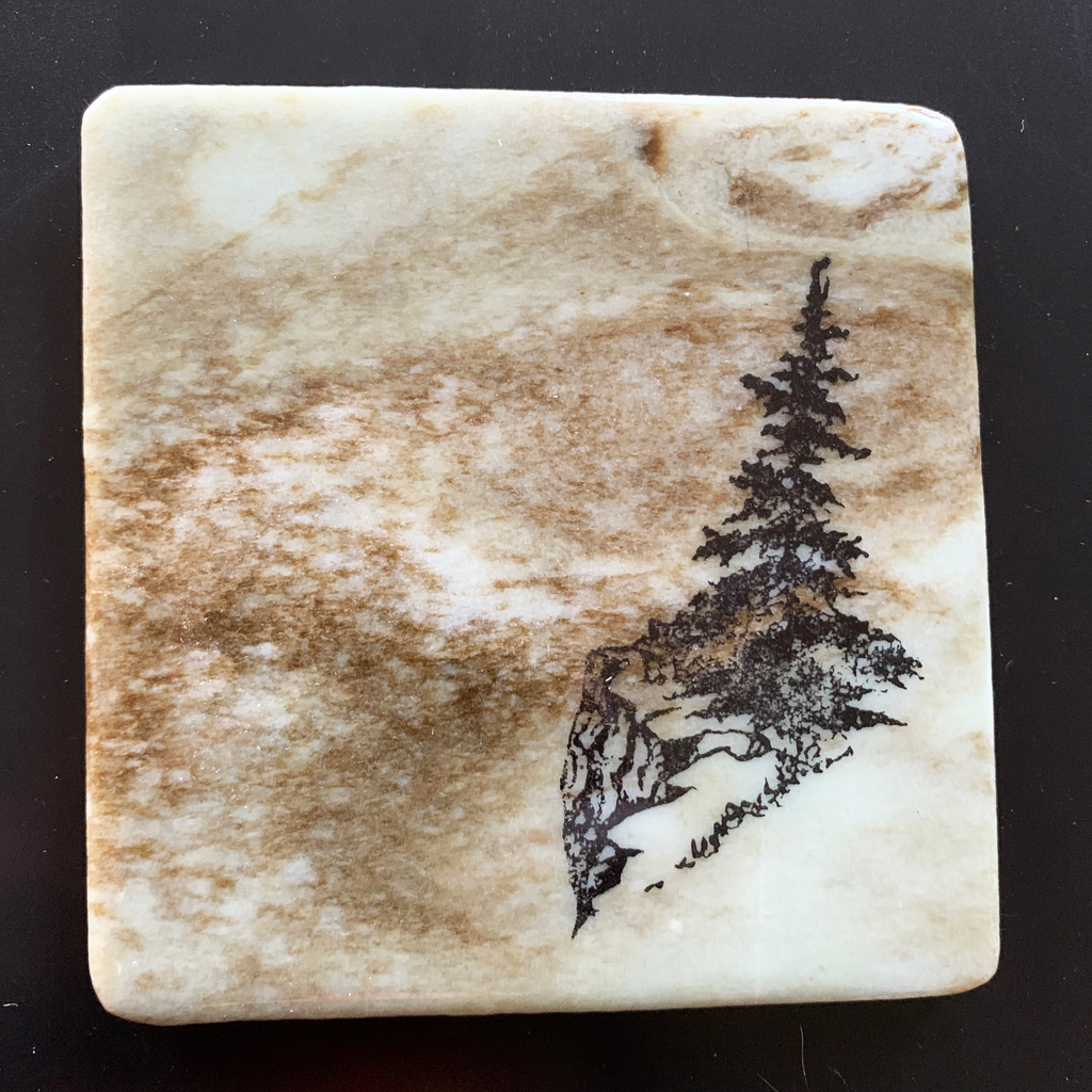 This coaster features the image of a pine tree on the edge of a rocky ledge with grass growing around it. The image is on a piece of canadian shield marble with mineral lines running through in unique colours, lines, and patterns. The coaster is finished with a clear coat, giving it a shiny finish. 