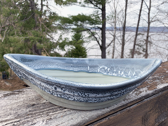 A grey and grey-green pottery boat with pointed ends, about the size of a small mixing bowl.