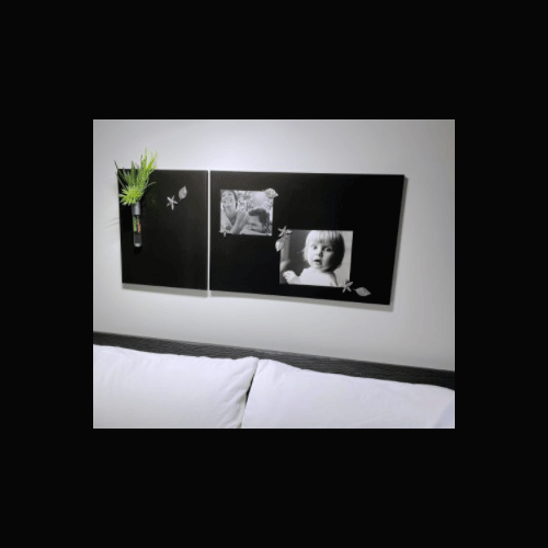 Two rectangular black boards hang on a wall above a couch. Seashell-themed magnets pin black and white pictures of a small child and a laughing couple to the board on the right. A colourful pen and two more beach-themed magnets are stored on the board on the left.