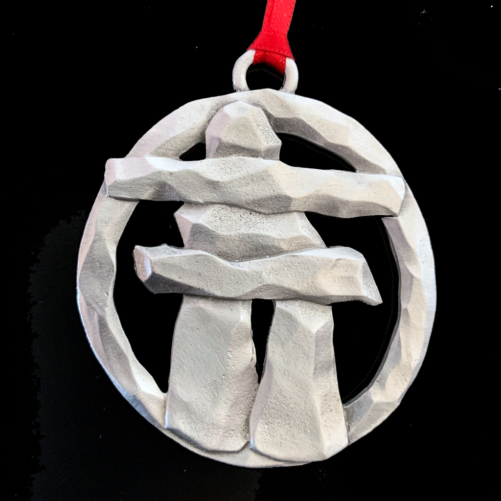An inukshuk stands with a frame encircling it, with a loop and red ribbon attached to the top. 