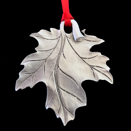 A maple leaf hangs upside down, its stem creating a loop for a red ribbon to be attached. 
