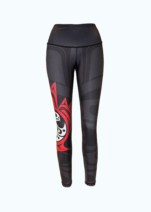 These black, grey, red and white leggings are decorated with a Haida eagle and maple leaf motif. The motif shows an eagle with one wing outstretched in front of it. It is enclosed by a red circle, which is itself enclosed by a maple leaf. A small red and white version of this motif is on the right leg. A larger grey version begins on the left leg and spreads across the entire leggings, though it is difficult to see against the black background. 