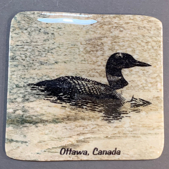 This coaster features the image of the sideview of a loon sitting on a lake with the words Ottawa, Canada below. The image is on a piece of canadian shield marble with mineral lines running through in unique colours, lines, and patterns. The coaster is finished with a clear coat, giving it a shiny finish.