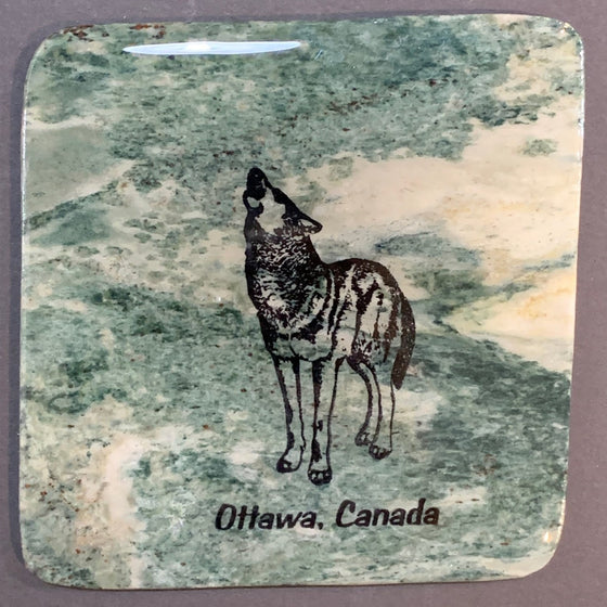 This coaster features the image of a wolf standing while howling into the sky, the words Ottawa, Canada below. The image is on a piece of canadian shield marble with mineral lines running through in unique colours, lines, and patterns. The coaster is finished with a clear coat, giving it a shiny finish.