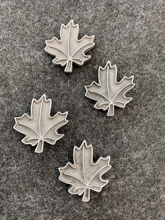 Four pewter magnets in the shape of maple leaves. Raised lines outline the outside of the leaf, and veins to the five points of the leaf. 