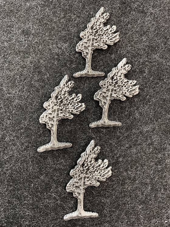 Four pewter magnets in the shape of windswept pine trees.