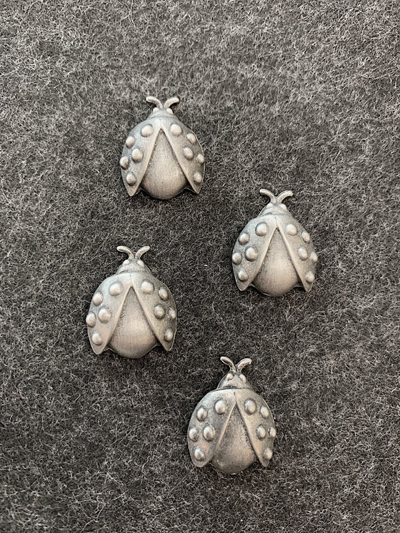 Four pewter magnets in the shape of ladybugs with spots on their open wing casings.