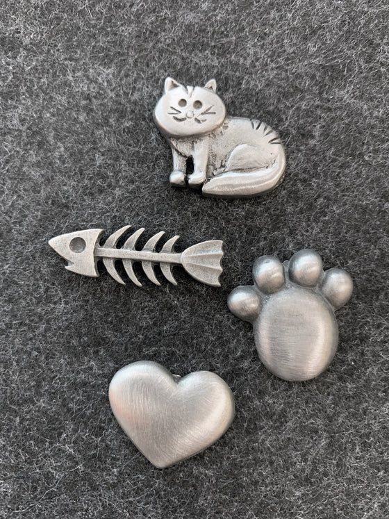This set of four pewter magnets includes a striped cat, a paw print, a heart, and a fish bone. 