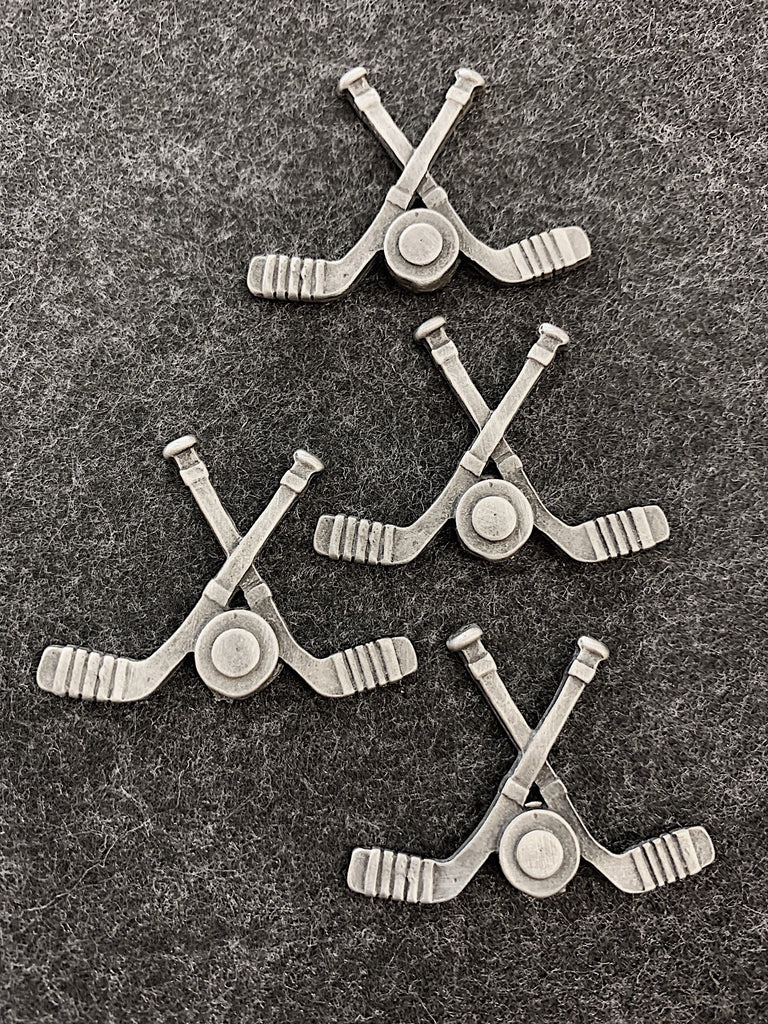 Four pewter magnets in the shape of two hockey sticks crossed with a puck between them. 
