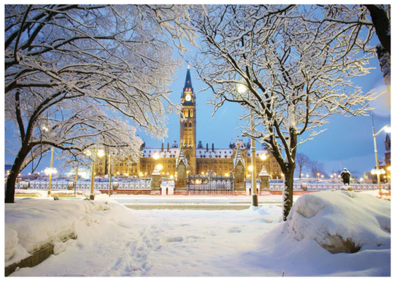Canada's Parliament Hill Centre Block on a winter evening with snow covered trees and a blue sky.