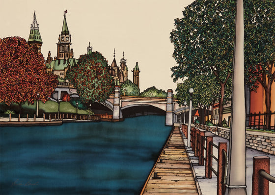 This rectangular magnet shows the Parliament building as seen from the Rideau Canal. The Parliament building is at the upper left of the picture and is partially obscured by trees, which are just beginning to develop their autumn colours. At the right of the picture is a boardwalk that follows the canal. The picture is richly coloured.